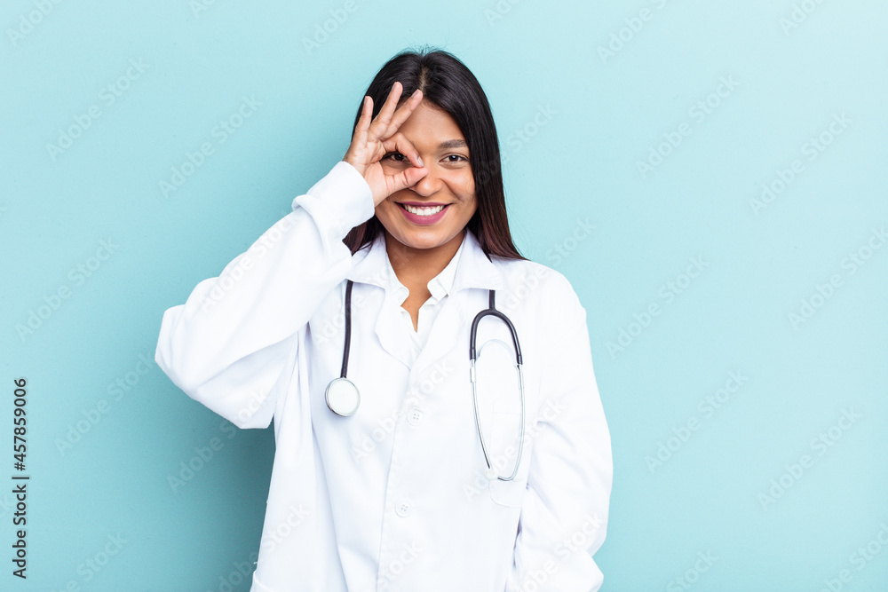 Young doctor Venezuelan woman isolated on blue background excited keeping ok gesture on eye. Young doctor Venezuelan woman isolated on blue background excited keeping ok gesture on eye.