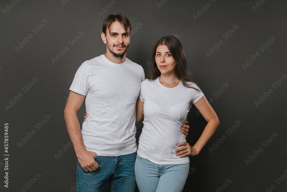 A young couple, a girl and a man in white blank t-shirts on a dark gray background. Mock-up. love story A young couple, a girl and a man in white blank t-shirts on a dark gray background. Mock-up. love story