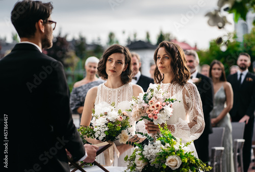 Portrait of two loving female lesbian LGBT brides telling their marriage vows at the wedding ceremony in front of wedding officiant. Shot with 2x anamorphic lens