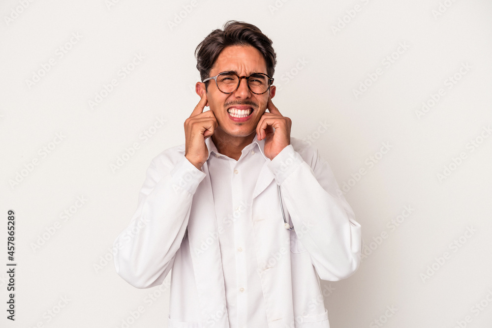Young mixed race doctor man isolated on white background covering ears with hands.