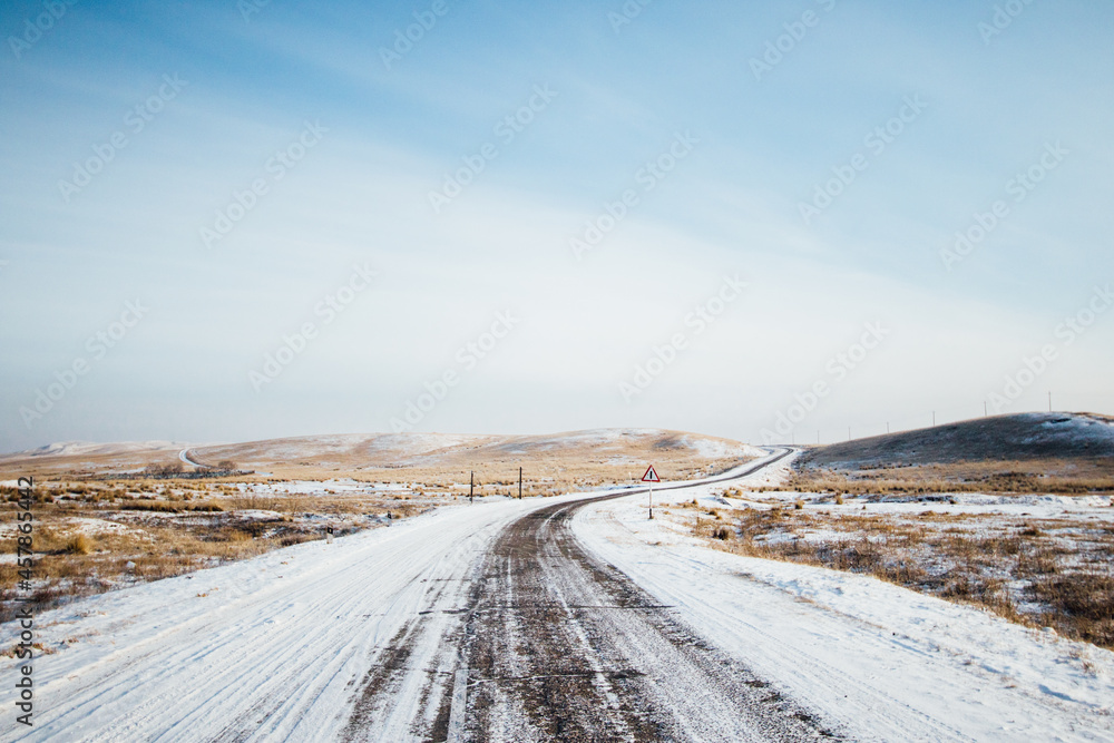 Snowy winter road in Khakassia with fields and mountains in the background Snowy winter road in Khakassia with fields and mountains in the background