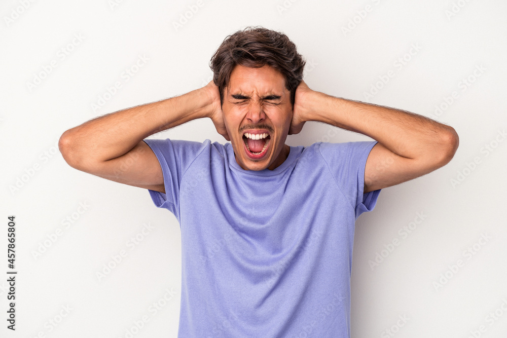 Young mixed race man isolated on white background covering ears with hands trying not to hear too loud sound. Young mixed race man isolated on white background covering ears with hands trying not to hear too loud sound.