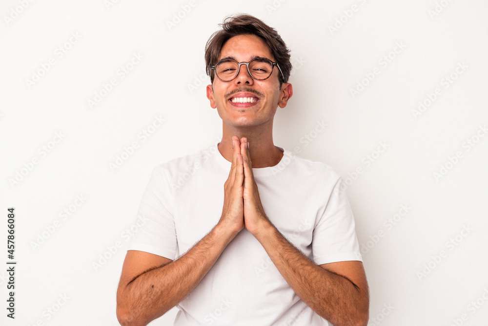 Young mixed race man isolated on white background holding hands in pray near mouth, feels confident. Young mixed race man isolated on white background holding hands in pray near mouth, feels confident.