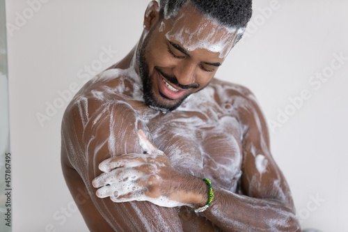 Close up cropped view young African man lather his muscular build body with hydrating shower gel, use natural quality fragrant bodycare wash product. Self hygiene, skincare, morning routine concept photo