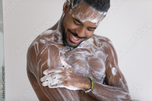 Fotografi Close up cropped view young African man lather his muscular build body with hydrating shower gel, use natural quality fragrant bodycare wash product