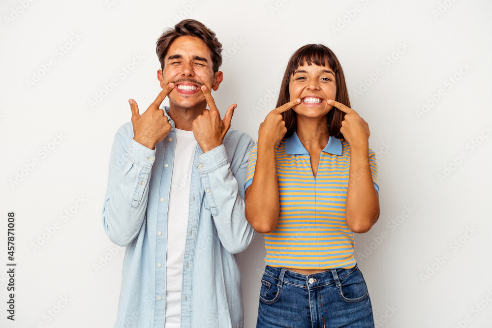 Young mixed race couple isolated on white background smiles, pointing fingers at mouth. Young mixed race couple isolated on white background smiles, pointing fingers at mouth.