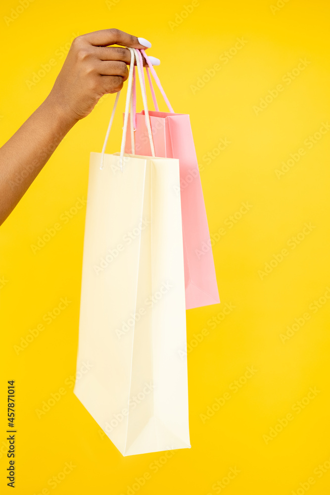 Shopping purchase. Black Friday. Sale discount. Closeup of African woman hand holding mall shopper bags isolated on orange background.