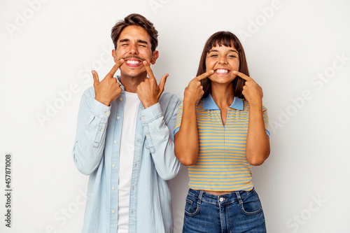 Young mixed race couple isolated on white background smiles, pointing fingers at mouth.
