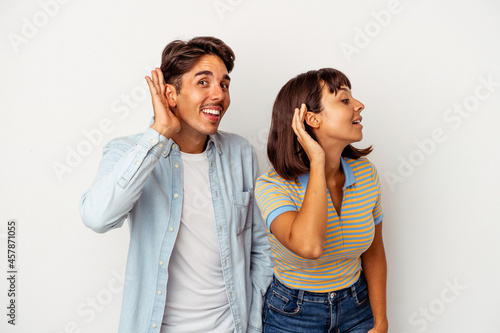 Young mixed race couple isolated on white background trying to listening a gossip.