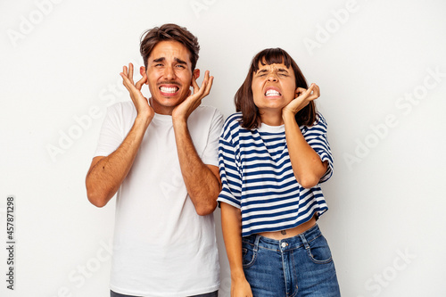 Young mixed race couple isolated on white background covering ears with hands.