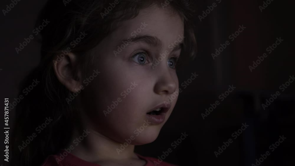 Portrait Сute Little Kid While Watching TV. Young Girl Watch Television on Living Room. Concept Video Game, Entertainment, Emotions, Family. Child Watching TV, Close up Face of Little Girl, Kid Eyes. Portrait Сute Little Kid While Watching TV. Young Girl Watch Television on Living Room. Concept Video Game, Entertainment, Emotions, Family. Child Watching TV, Close up Face of Little Girl, Kid Eyes.