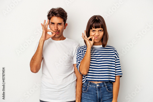 Young mixed race couple isolated on white background with fingers on lips keeping a secret.