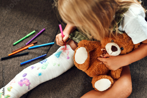 Little girl with a broken leg on the couch. The child draws with felt-tip pens on a plaster bandage. photo