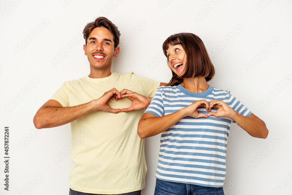 Young mixed race couple isolated on white background smiling and showing a heart shape with hands. Young mixed race couple isolated on white background smiling and showing a heart shape with hands.
