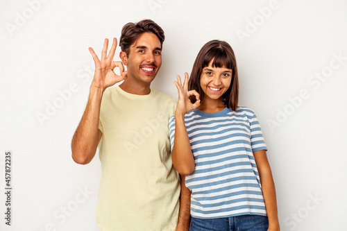 Young mixed race couple isolated on white background cheerful and confident showing ok gesture.