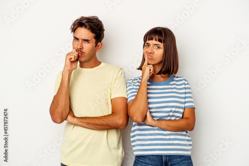 Young mixed race couple isolated on white background unhappy looking in camera with sarcastic expression.