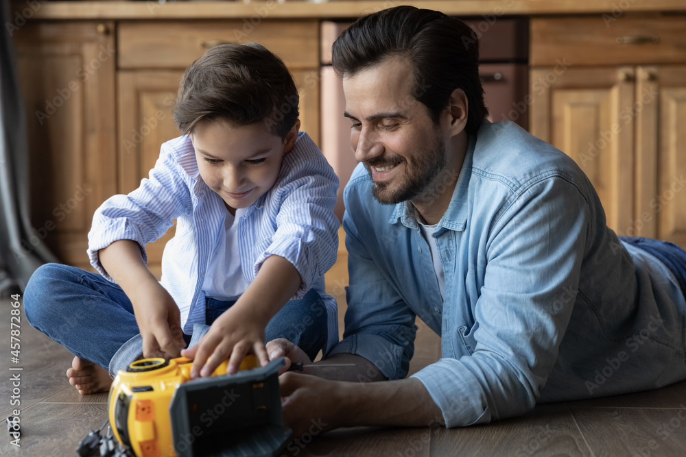 Close up happy father with little son fixing toy car, relaxing on wooden floor at home, caring loving dad helping to 8s boy kid with broken plastic truck, family enjoying leisure time together Close up happy father with little son fixing toy car, relaxing on wooden floor at home, caring loving dad helping to 8s boy kid with broken plastic truck, family enjoying leisure time together