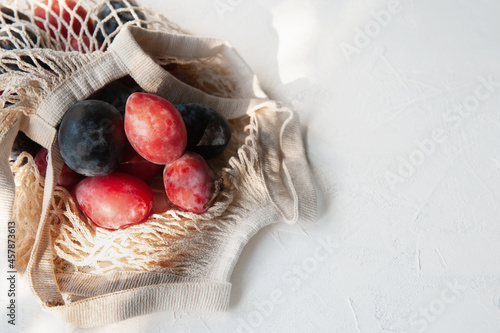 Fresh plums with leaves on a reusable mesh shopping bag. Flat lay, autumn background. Ripe organic plums and nectarines in an eco string bag. Soft focus. Zero waste concept.