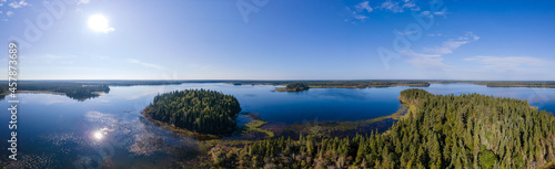 Aerial panorama of a large dark blue lake that is surrounded by trees. The sun is in the photo. 
