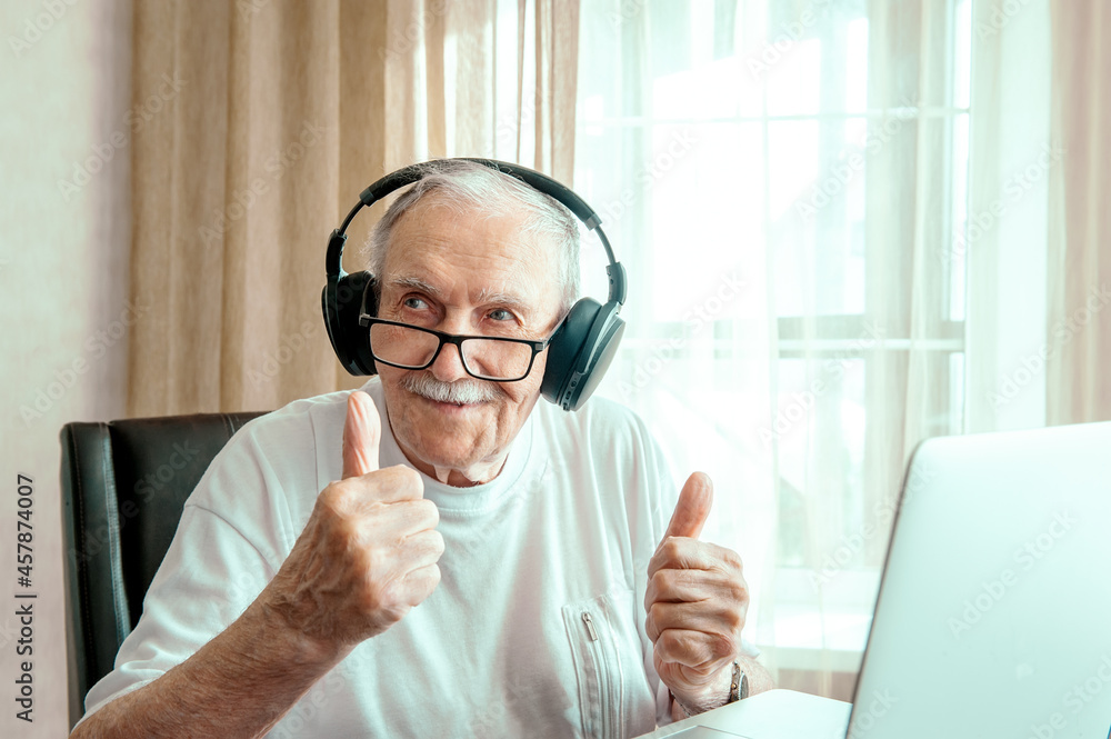 portrait of an elderly man with headphones. Positive human emotions, facial expression. A smiling elderly man using a laptop at home, listening to his favorite music and looking for information 