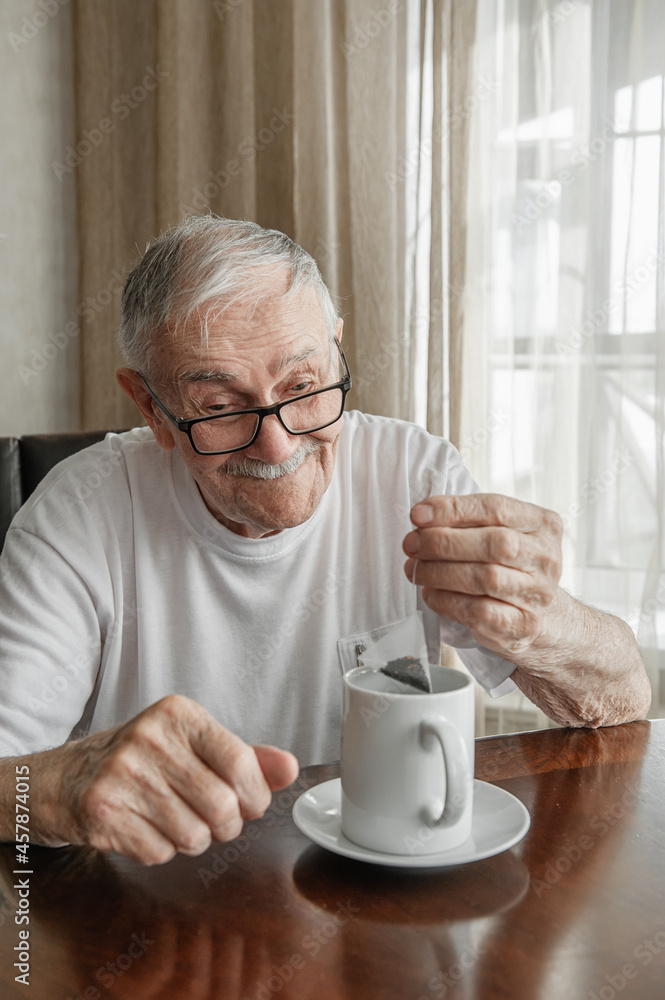 gray-haired, cheerful old man is brewing a tea bag in a cup. Portrait of an old man who drinks tea gray-haired, cheerful old man is brewing a tea bag in a cup. Portrait of an old man who drinks tea