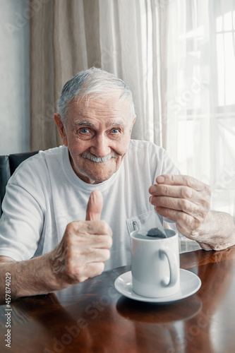 gray-haired, cheerful old man is brewing a tea bag in a cup. Portrait of an old man who drinks tea