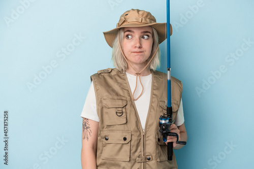 Young caucasian fisherwoman holding a rod isolated on blue background confused, feels doubtful and unsure.