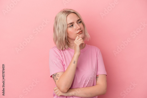 Young caucasian woman isolated on pink background thinking and looking up, being reflective, contemplating, having a fantasy.