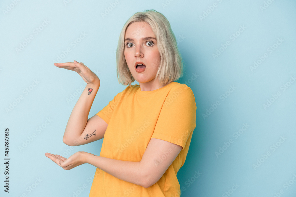 Young caucasian woman isolated on blue background shocked and amazed holding a copy space between hands. Young caucasian woman isolated on blue background shocked and amazed holding a copy space between hands.