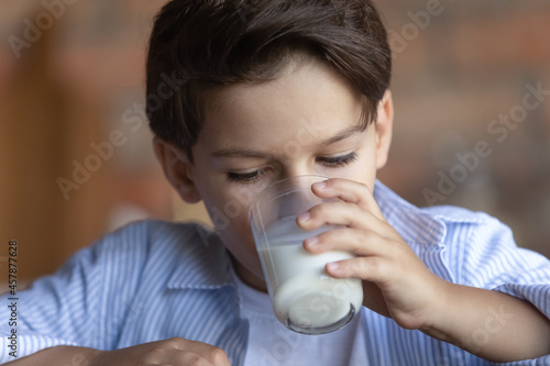 Close up healthy Caucasian 8s boy drinking tasty fresh milk, holding glass, child enjoying organic food yogurt, little preschooler kid getting vitamins and calcium, children healthcare concept