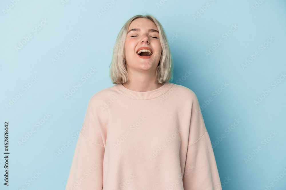 Young caucasian woman isolated on blue background relaxed and happy laughing, neck stretched showing teeth. Young caucasian woman isolated on blue background relaxed and happy laughing, neck stretched showing teeth.