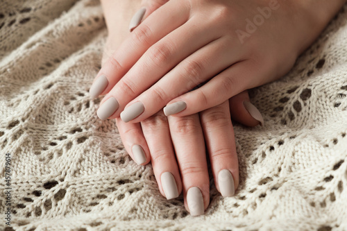 Matt nude beige nails close up. Winter or autumn manicure, woman hand on warm sweater