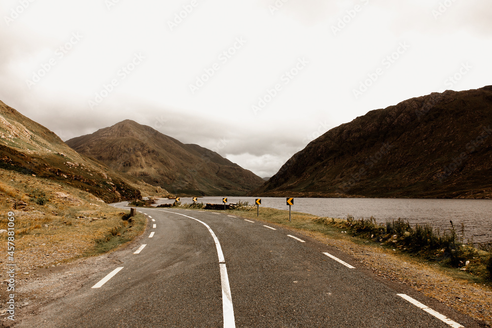 Fototapeta premium An empty rural road and a stunning landscape in Ireland. Mountains, hills and a lake next to the road. 