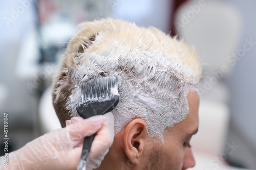 Hair dyeing for a young man in a hairdressing salon. the master bleaches the hair