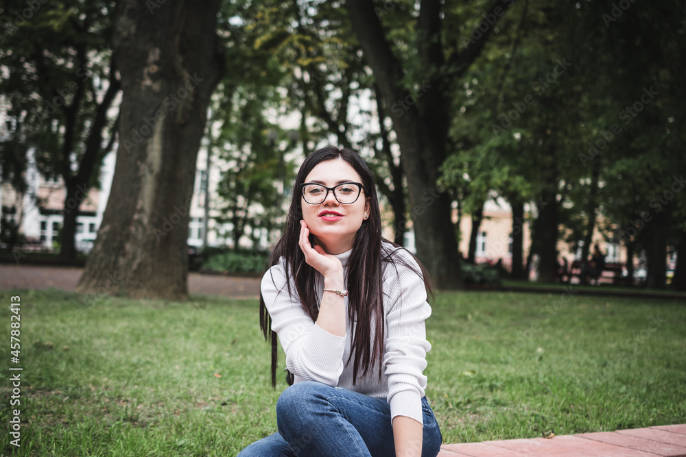 Beautiful stylish girl in jeans and a white sweater outdoors in the park with a phone Beautiful stylish girl in jeans and a white sweater outdoors in the park with a phone