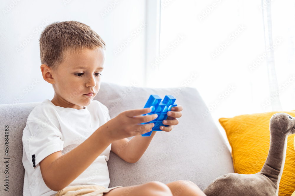 Soft stuffed toys with bubbles. Child plays with blue pop-it in form of puzzle. Cheerful boy holds in his hands a blue toy anti-stress pop it. Soft stuffed toys with bubbles. Child plays with blue pop-it in form of puzzle. Cheerful boy holds in his hands a blue toy anti-stress pop it.