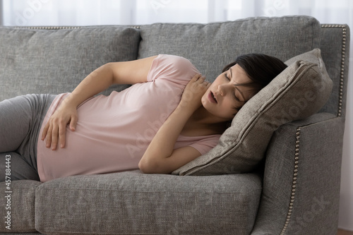 Future mother napping. Exhausted expectant mom lie on sofa with closed eyes get some sleep in comfortable pose hold hand on big tummy. Young pregnant female rest fall asleep on couch hugging baby bump