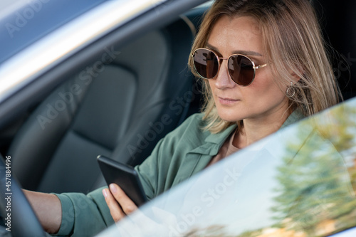 Young contemporary woman driving car and texting in smartphone in the morning
