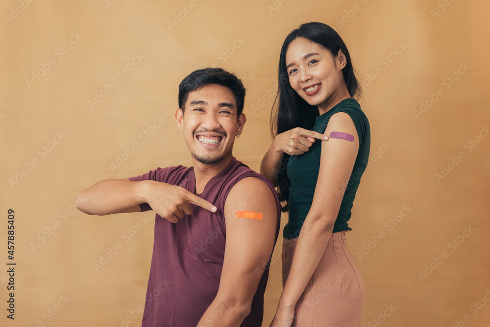Fototapeta premium Asian man and woman showing shoulders after getting a vaccine. Happy couple showing arm with band-aids on after vaccine injection.