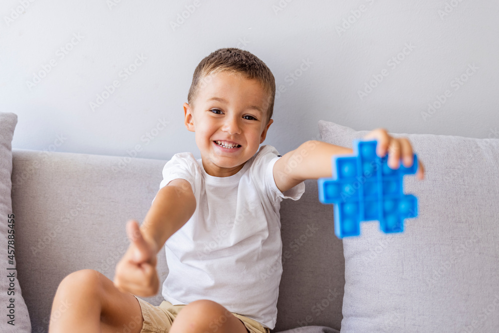 Boy smiling and playing with blue pop it fidget toy. Push bubble fidget sensory toy - washable and reusable stress relief toy. Antistress toy for child with special needs. Mental health concept Boy smiling and playing with blue pop it fidget toy. Push bubble fidget sensory toy - washable and reusable stress relief toy. Antistress toy for child with special needs. Mental health concept