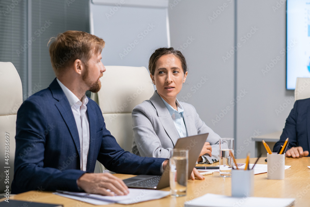 Two contemporary business people discussing conference points by desk Two contemporary business people discussing conference points by desk