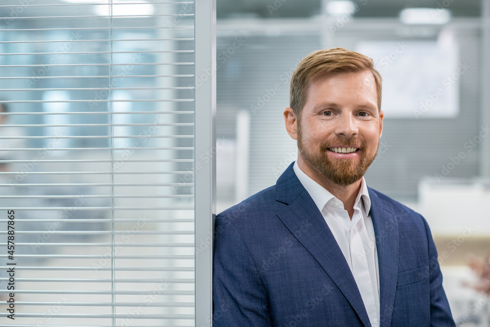 Business leader with toothy smile standing against office interior in front of camera Business leader with toothy smile standing against office interior in front of camera
