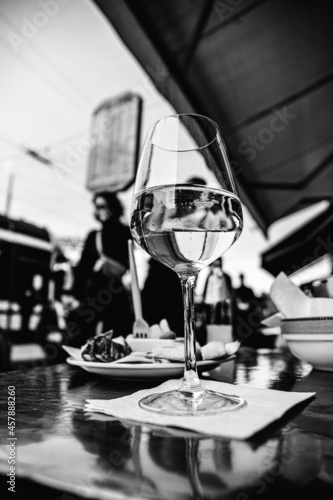 Close up shot from below of a glass of white wine on the table of a cocktail bar in the city. Happy hour or aperitif time in busy downtown Milan.