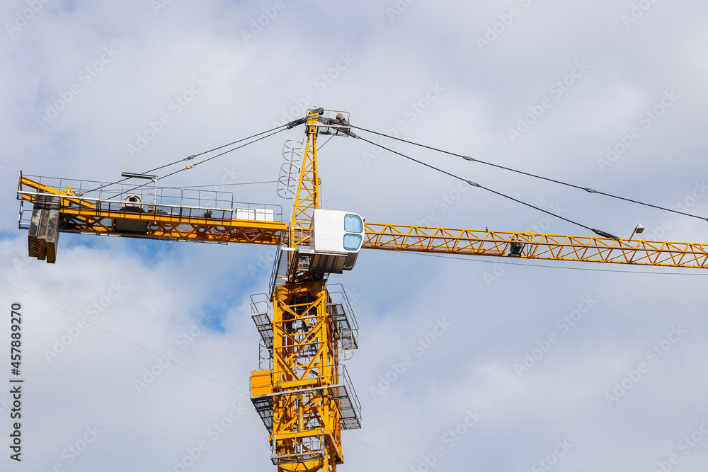 Yellow tower crane. Construction site with crane. Construction crane at blue sky background. Tower crane against blue sky with clouds. Tower crane working at construction site. Yellow tower crane. Construction site with crane. Construction crane at blue sky background. Tower crane against blue sky with clouds. Tower crane working at construction site.