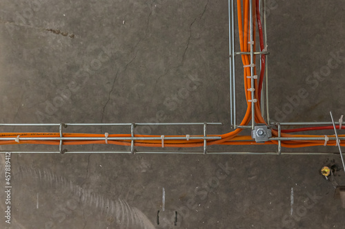 Cable tray with orange wires and metal duct show above t-bar grid below concrete of upper floor at construction site of building. Fire extinguishing and fire alarm system orange wires photo