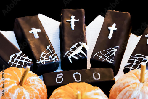 Large chocolates decorated with children's drawings of white icing sugar in the theme of Halloween. Crosses and cobwebs on cakes covered with brown chocolate. Decorating food Halloween.