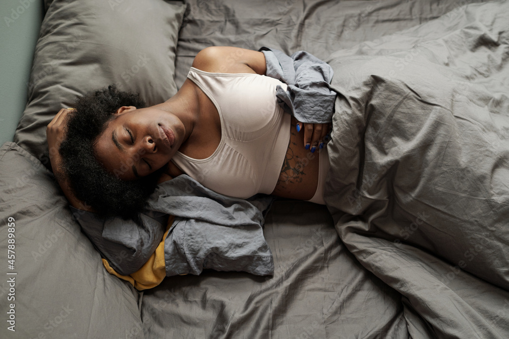 Fototapeta premium Young tired female sleeping under grey blanket on large bed after hard day