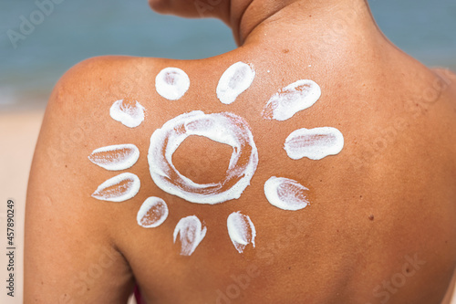 Woman Applying Sun Cream on Tanned Shoulder In Form Of The Sun. Sun Protection.Sun Cream. Skin and Body Care. Girl Using Sunscreen to Skin. Female Holding Suntan Lotion and Moisturizing Sunblock.