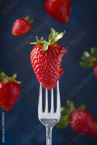 Fresa con mordida de lado derecho sobre un cubierto de mesa a detalle con fondo azul y fresas desenfocadas en el fondo photo