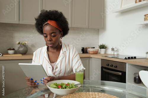 Serious businesswoman with tablet having vegetarian breakfast by kitchen table